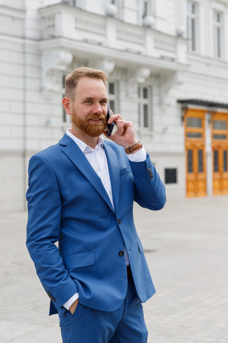 Adwokat Sławomir Wojciulewicz przed gmachem sądu rozmawiający przez telefon. Ubrany w niebieski garnitur z zegarkiem na lewej ręce