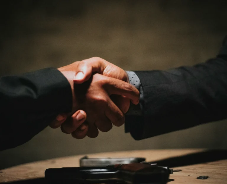 Dwie uściśnięte dłonie nad leżącym na stole pistoletem i magazynkiem