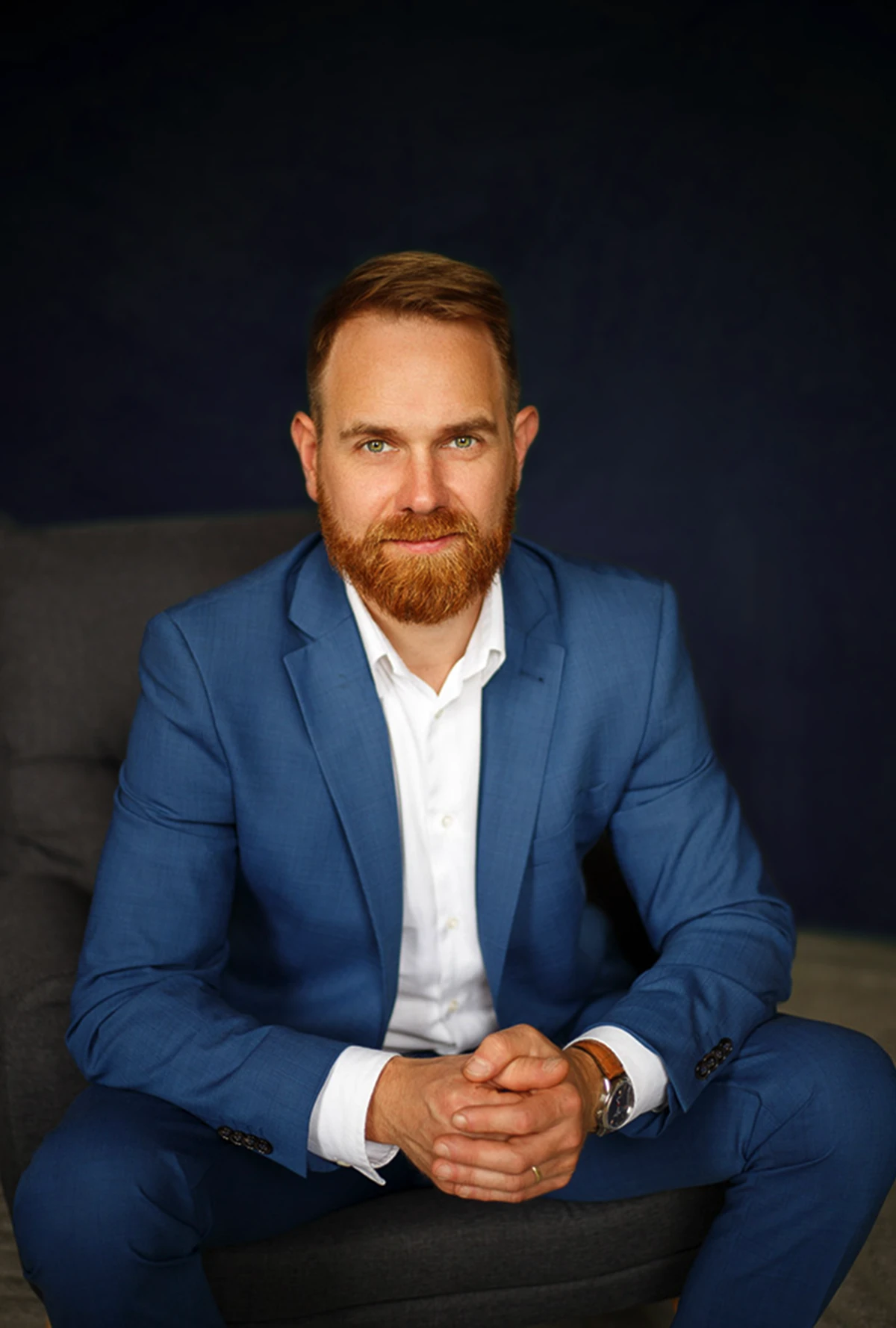 Adwokat Sławomir Wojciulewicz siedzący na kanapie. Ubrany w elegancki niebieski garnitur i białą koszulę.